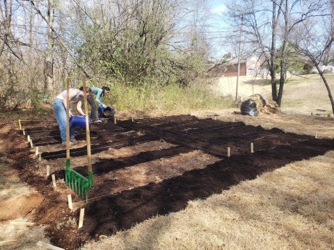 Community garden with freshly tilled soil, ready for planting, located at Cedar Bluff Middle School. Volunteers are preparing the garden beds for planting vegetables and flowers.