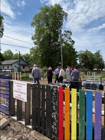 A diverse group of community members gathers outdoors at Knox County Community Garden & Growers Alliance. The event features vibrant, colorful pallet decorations and a welcoming atmosphere for local gardeners.
