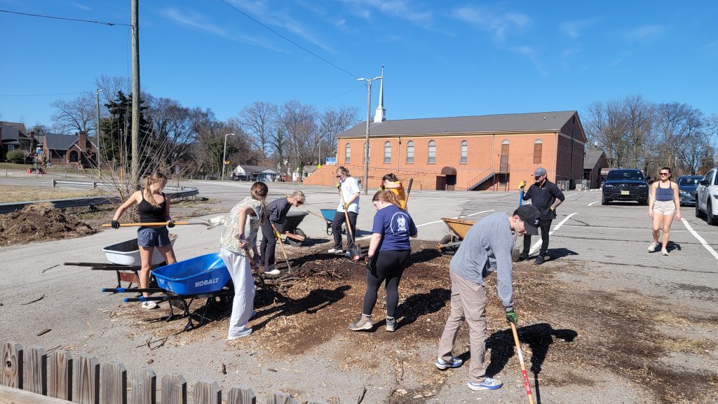 Group of diverse volunteers planting and tending a community garden outdoors on a sunny day.