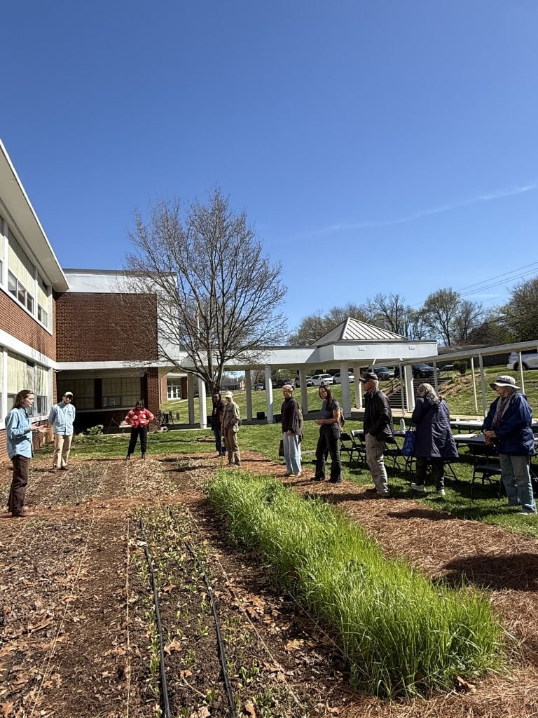 Group of diverse community members gathered in a community garden at Knox County Growers Alliance, participating in a gardening or educational event on a sunny day.