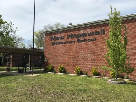 View of the Knox County Community Garden at New Hopewell Elementary School, featuring a brick building with the school name and surrounding greenery.