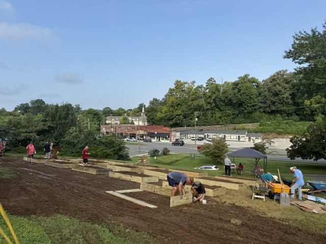 Community members working together to build a community garden in Knox County, with trees and buildings in the background.