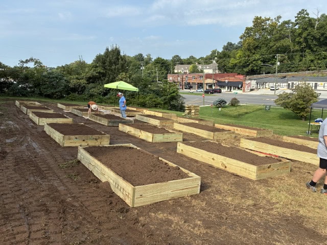 Newly built wooden garden beds in Knox County community garden with people working and a person with an umbrella in the background.