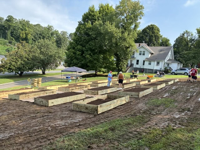People working on building raised garden beds in a community garden with trees and houses in the background.