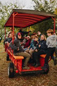 Group of diverse people enjoying a pedal-powered vehicle ride outdoors in a park setting with trees and autumn foliage.